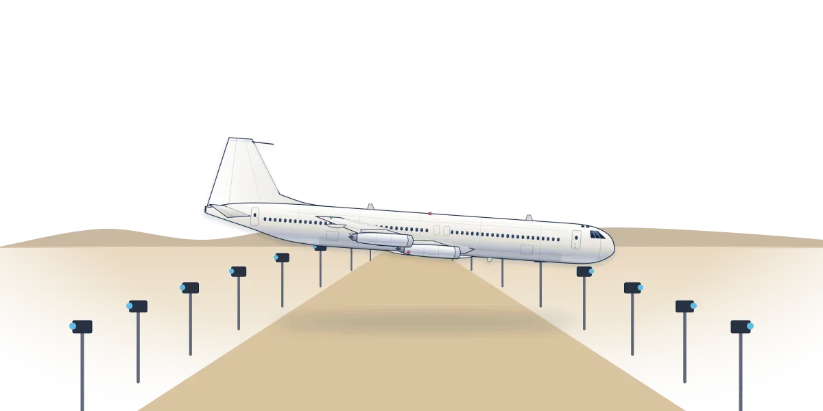 A four-engine jet skimming low over a desert lakebed toward a strip lined with cameras on poles