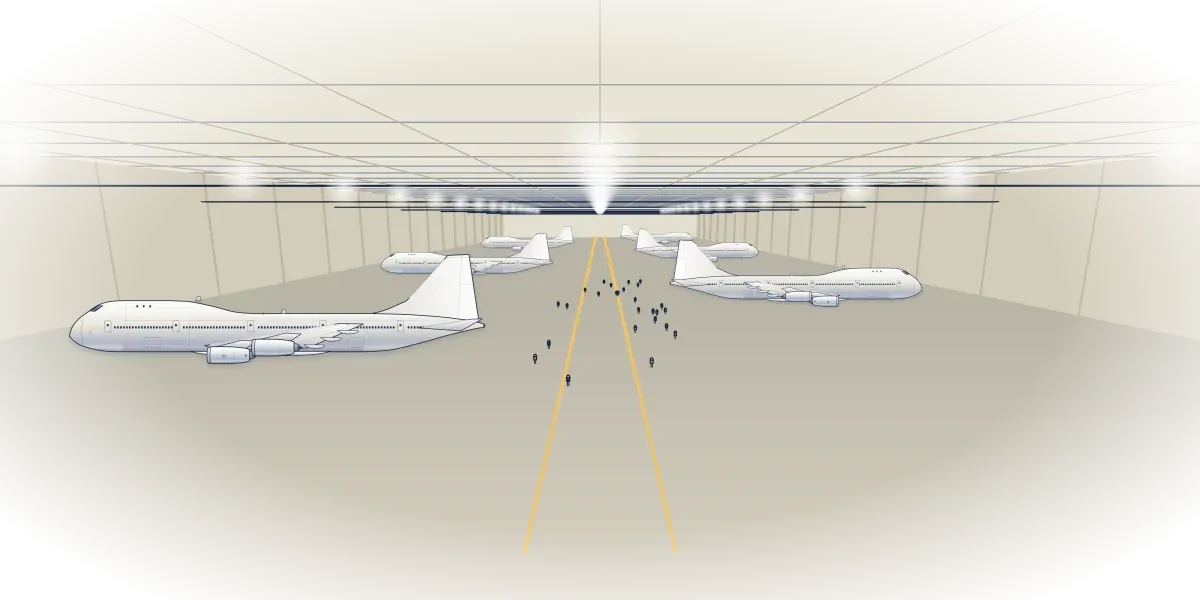 A vast factory hall with several 747s parked under rows of lights and tiny workers walking between them