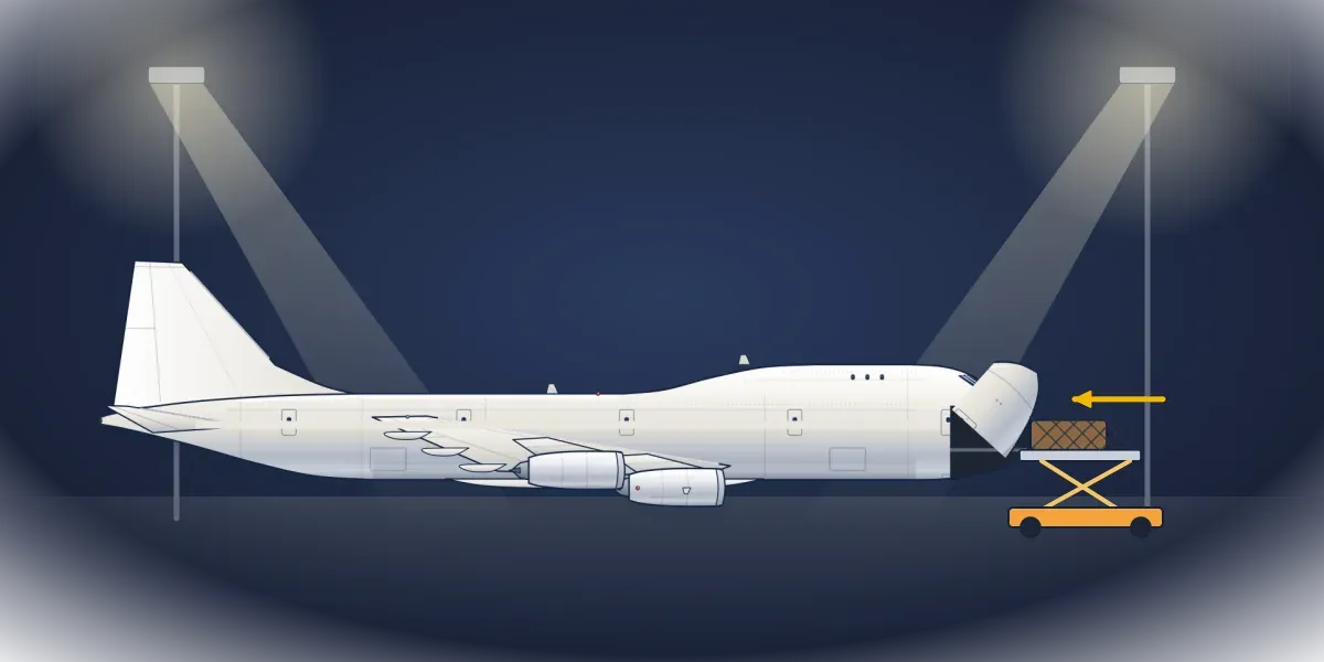 A 747 freighter under floodlights with its nose hinged upward and a cargo loader lifting a pallet toward the opening
